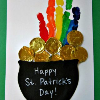 A photo of a kids St Patrick's Day handprint craft with a rainbow handprint coming out of a pot of gold, which is made out of black construction paper and chocolate gold coin wrappers.