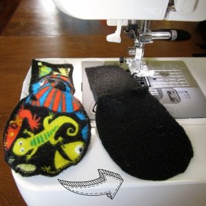 Fabric and felt pieces for a homemade kids eye patch sitting alongside a sewing machine with an arrow indicating how to sandwich the pieces together for sewing.