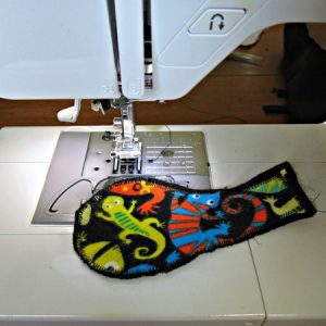 Fabric and felt pieces in the shape of eyeglasses' lense and temple being sewn together on a sewing machine.