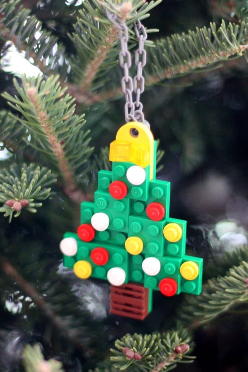 A n easy LEGO ornament idea for preschoolers featuring a Christmas tree-shaped ornament made out of green, brown, red, yellow, and white LEGO bricks.