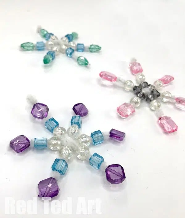 A photo of a group of DIY beaded snowflake ornaments, an easy ornament idea for preschoolers using pipe cleaners and sparkly pastel beads.