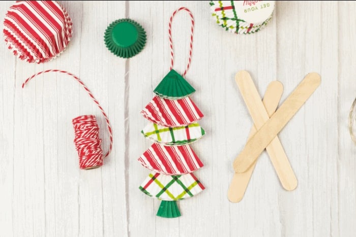 A photo of a homemade ornament craft for preschoolers that uses red and green patterned cupcake liners folded and layered on a craft stick to look like a little Christmas tree.