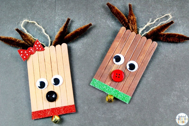 A photo of 2 cute reindeer Christmas ornament crafts made out of brown popsicle sticks with pipe cleaner antlers, googly eyes, and red button nose.