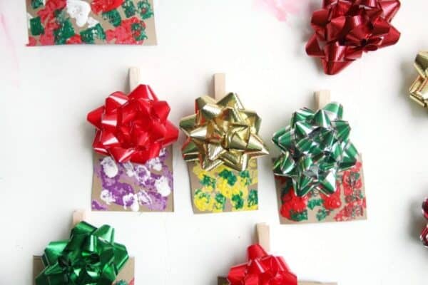 A photo of 3 homemade Christmas ornaments made out of painted cardboard and Christmas bows to look like mini Christmas gifts.
