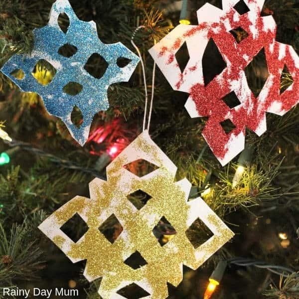 A photo of a group of sparkly glittered paper snowflake ornaments hanging on a Christmas tree.
