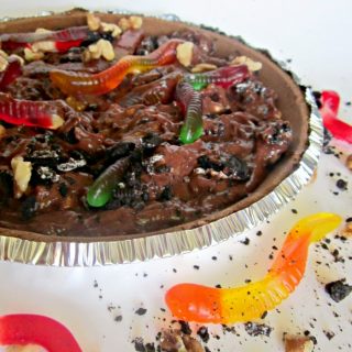 A photo of a kids dessert mud pie with chocolate pudding, Oreo cookie crumbs, chopped walnuts, and gummy worms.