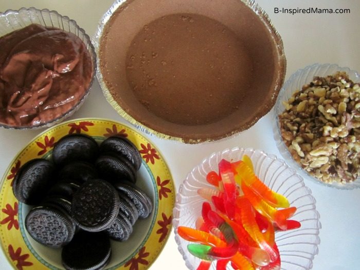 A photo of a kids Mud Pie recipe ingredients, including a chocolate cookie crumb pie crust, chocolate pudding, chopped walnuts, Oreo cookies, and gummy worms. 