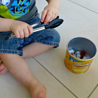A photo of a toddler doing a tongs and pom poms activity.