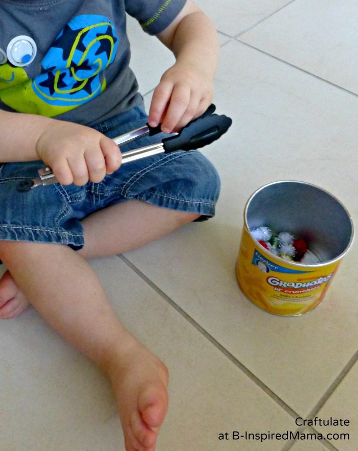 A photo of a toddler doing a tongs and pom poms activity.
