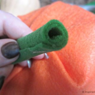A hand holding a handmade pumpkin stem made out of rolled-up green felt.