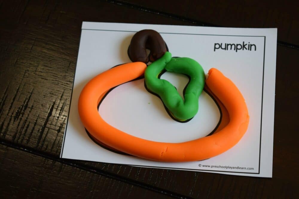 A photo of playdough snakes placed on the lines of a printable pumpkin playdough card to form a pumpkin shape.