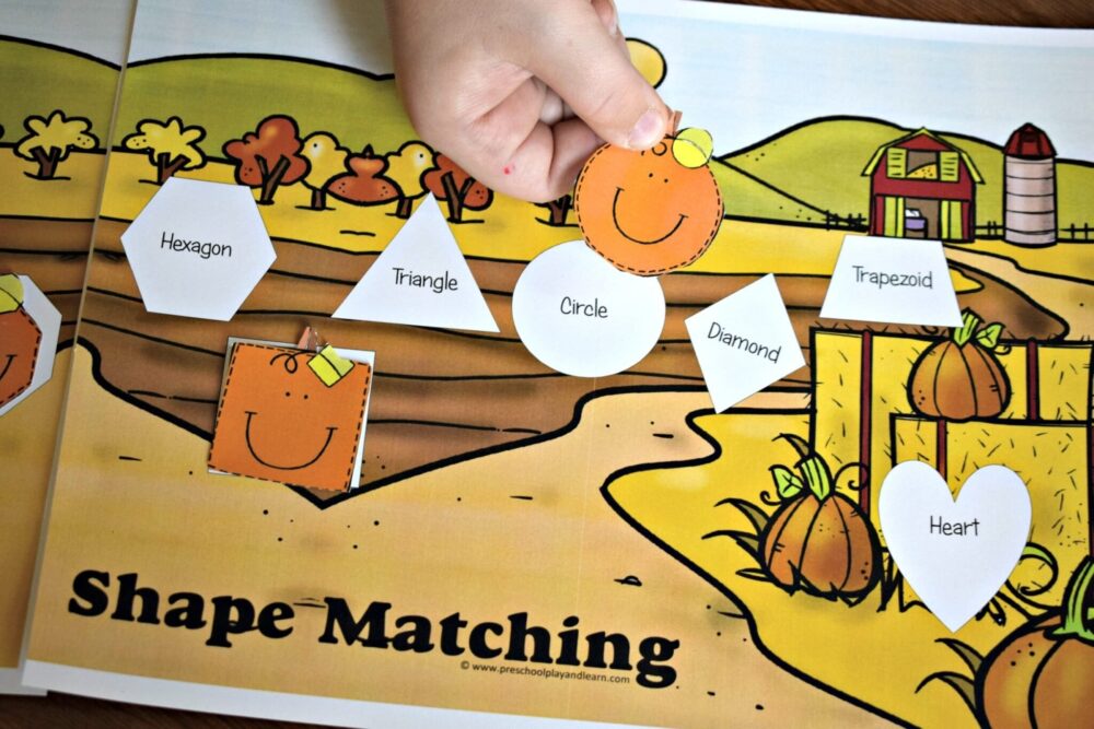 A photo of a preschool child's hand matching a circle-shaped paper pumpkin with a matching white circle on a printable pumpkin patch sheet.