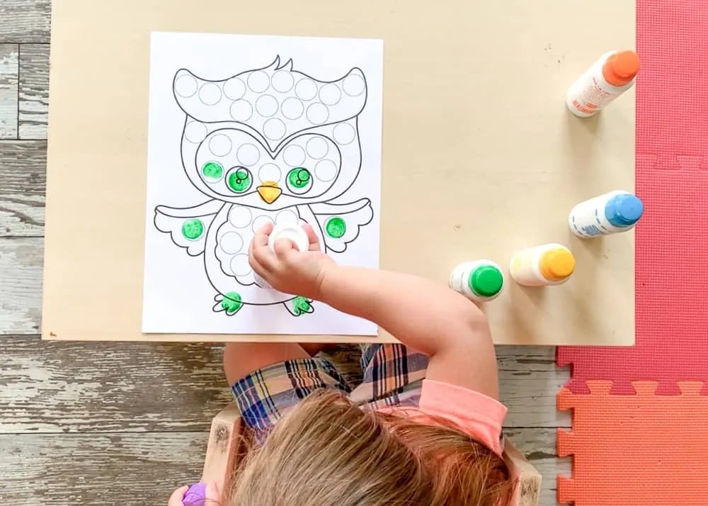 A photo of a young preschool child using dot markers to color a cute printable owl coloring page for Fall.