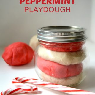 A photo of red and white Candy Cane Peppermint Playdough layered in a small mason jar alongside two candy canes.