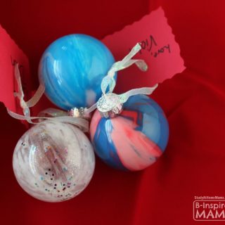 Three DIY pour painting Christmas balls, homemade Christmas ornaments easy enough for kids. One features colorful glitter and white paint inside a clear plastic fillable ornament. Another features light blue and white paint swirled inside a clear plastic ball ornament. The last one features red, pink, and blue paint swirled inside a clear plastic ball ornament.