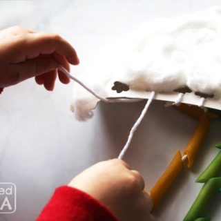 photo of a preschool child's hands tying strings onto a rainbow mobile.