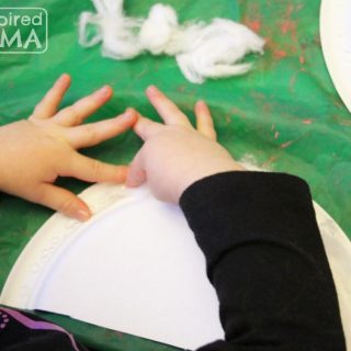 A photo of a preschooler gluing cotton balls onto a half of a paper plate while making a rainbow mobile craft.
