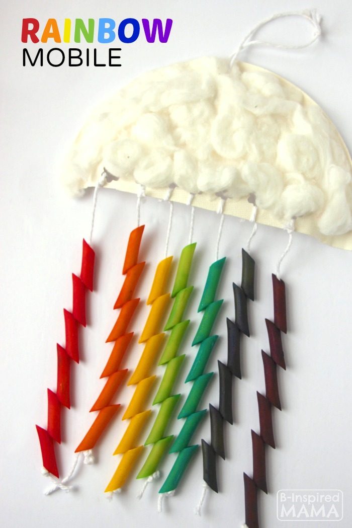 A photo of a cute and colorful Rainbow Mobile Craft for Kids featuring a half of a paper plate covered in white cotton balls to look like a cloud with strings hanging down that are threaded with dyed pasta.