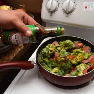 A photo of a step in the process of making a quick Smoked Sausage and Rice Skillet Recipe, including a hand pouring from a bottle of soy sauce into a frying pan filled with sliced smoked sausage and broccoli.