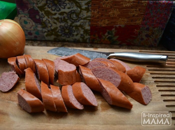 A photo of a step in the process of making a quick Smoked Sausage and Rice Skillet Recipe, including smoked sausage, cut into 1-inch slices, on a wooden cutting board next to a knife.