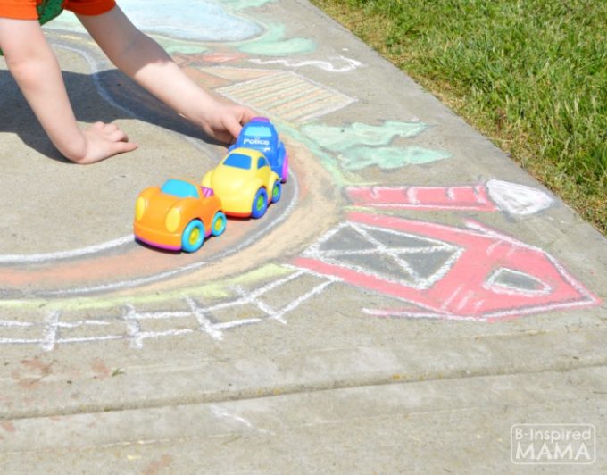 A photo of a child pushing plastic toy cars along a sidewalk chalk art road through a chalk town with a farm and barn.