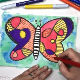 A photo of a hand using markers to draw patterns inside the wings of a kids watercolor butterfly painting.