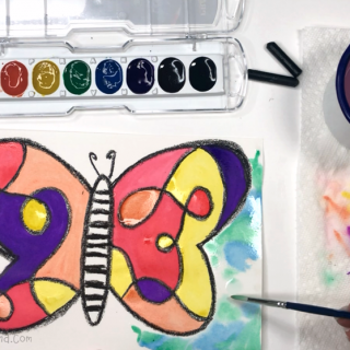 A photo of a hand painting the background of a colorful watercolor butterfly painting for kids.