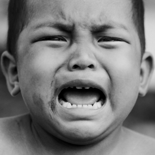 A photo of an overly emotional child crying with their mouth open and eyes squinting.