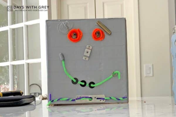 A photo of a kid-made robot costume for Halloween, made out of a cardboard box, found objects, and silver spray paint.