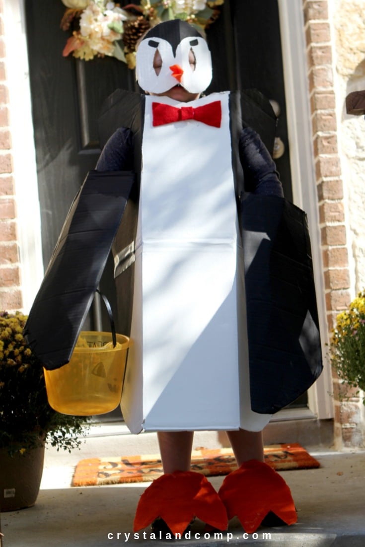 A child stands outside wearing a DIY creative Halloween costume that looks like a penguin and is made out of painted cardboard and felt.