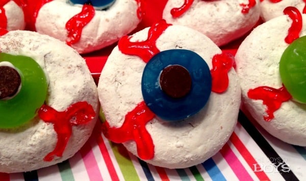 A photo of creepy donut eyeballs Halloween treats for kids consisting of white powder mini donuts with blue and green Lifesavers Gummies and chocolate chips in the center along with red gel icing veins.