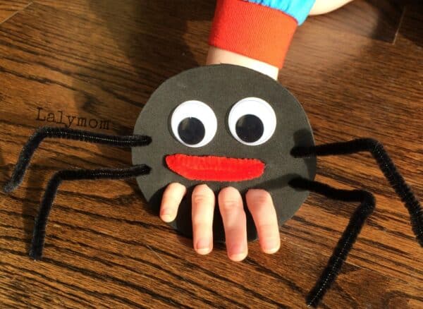 A photo of a child's hand using a cute homemade spider finger puppet made out of black cardstock, big googly eyes, and black pipe cleaner legs.