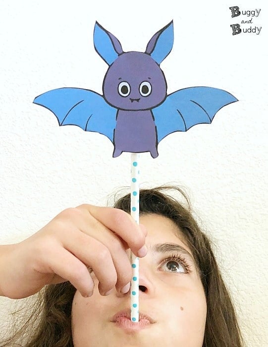 A photo of a child blowing through the straw of a printable flying bat Halloween craft.