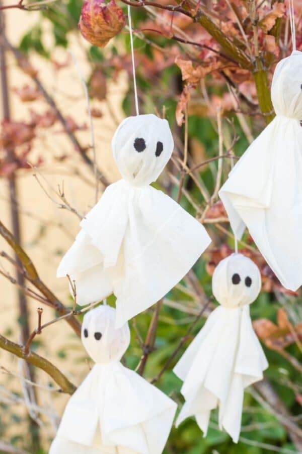 A photo of spooky ghost lollipops hanging from tree branches, a Halloween Party Craft for kids to make.