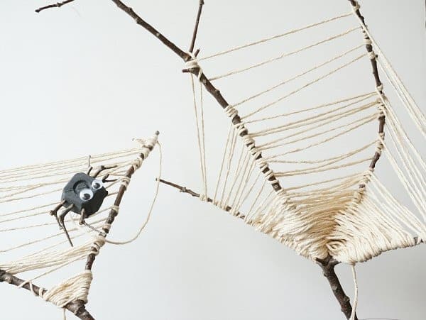 A photo of a DIY twig spider web Halloween party craft using real twigs, white string, and a fake spider.