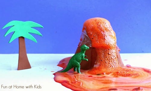A cute non-candy Valentine idea with everything a child needs to do a fun erupting volcano science experiment including a brown foam sheet volcano with red bubbly liquid spilling out and a small plastic dinosaur toy.