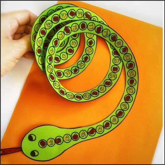 A photo of a child's hand holding a swirling green paper snake with numbered dots along it, made using a free 100th day of school printable craft.