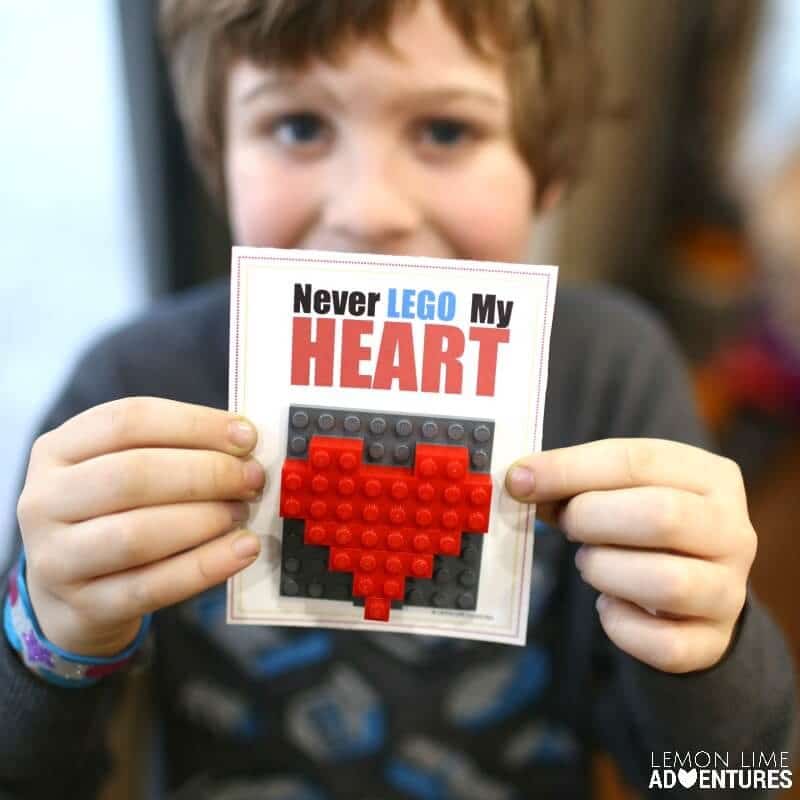A happy child holding a DIY printable Valentine with a red LEGO heart attached to it and the saying "Never LEGO my heart."