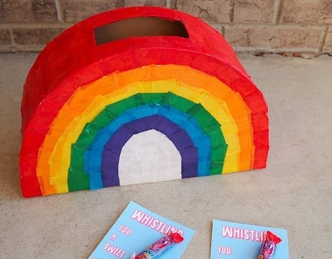 A colorful rainbow Valentine mailbox idea for kids featuring a rainbow-shaped Valentine box with tissue paper squares glued on for the rainbow colors of red, orange, yellow, green, blue, and purple.