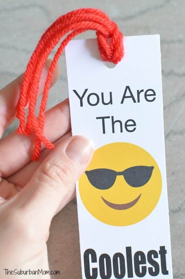 A hand holding a printable bookmark Valentine featuring a yellow smiling emoji and the saying, "You Are The Coolest!"