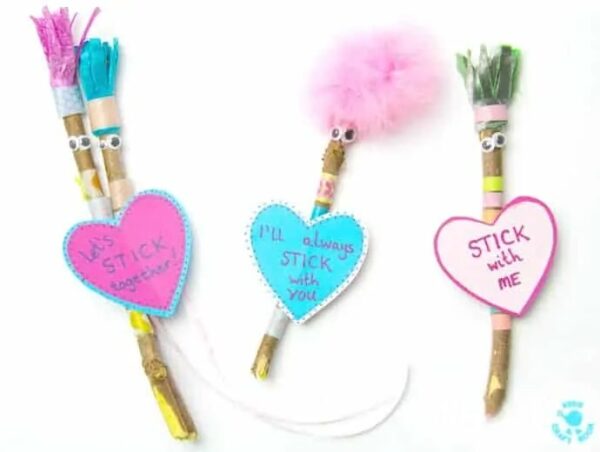 Four cute stick-figure Valentines made with googly eyes, patterned washi tape, feathers, and felt on small sticks with paper heart tags tied onto them. A fun and crafty non candy Valentine idea for kids.