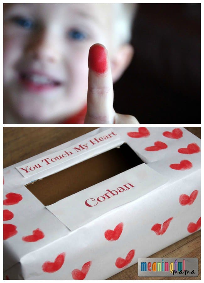 A collage of two photos of a sweet fingerprint hearts Valentines mailbox craft, with the top photo being a smiling child holding up a red paint-covered pointer finger and the bottom photo showing a white paper-covered tissue box decorated with little red hearts made out of a child's fingerprints and printed labels reading "You touch my heart" and the child's name, "Corban."