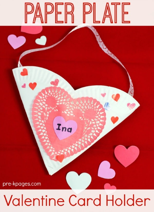 An easy paper plate heart Valentine holder idea featuring a heart-shaped pocket made out of two folded white paper plates, decorated with heart stickers and a red heart paper doily and with pink ribbon attached to the top for hanging.